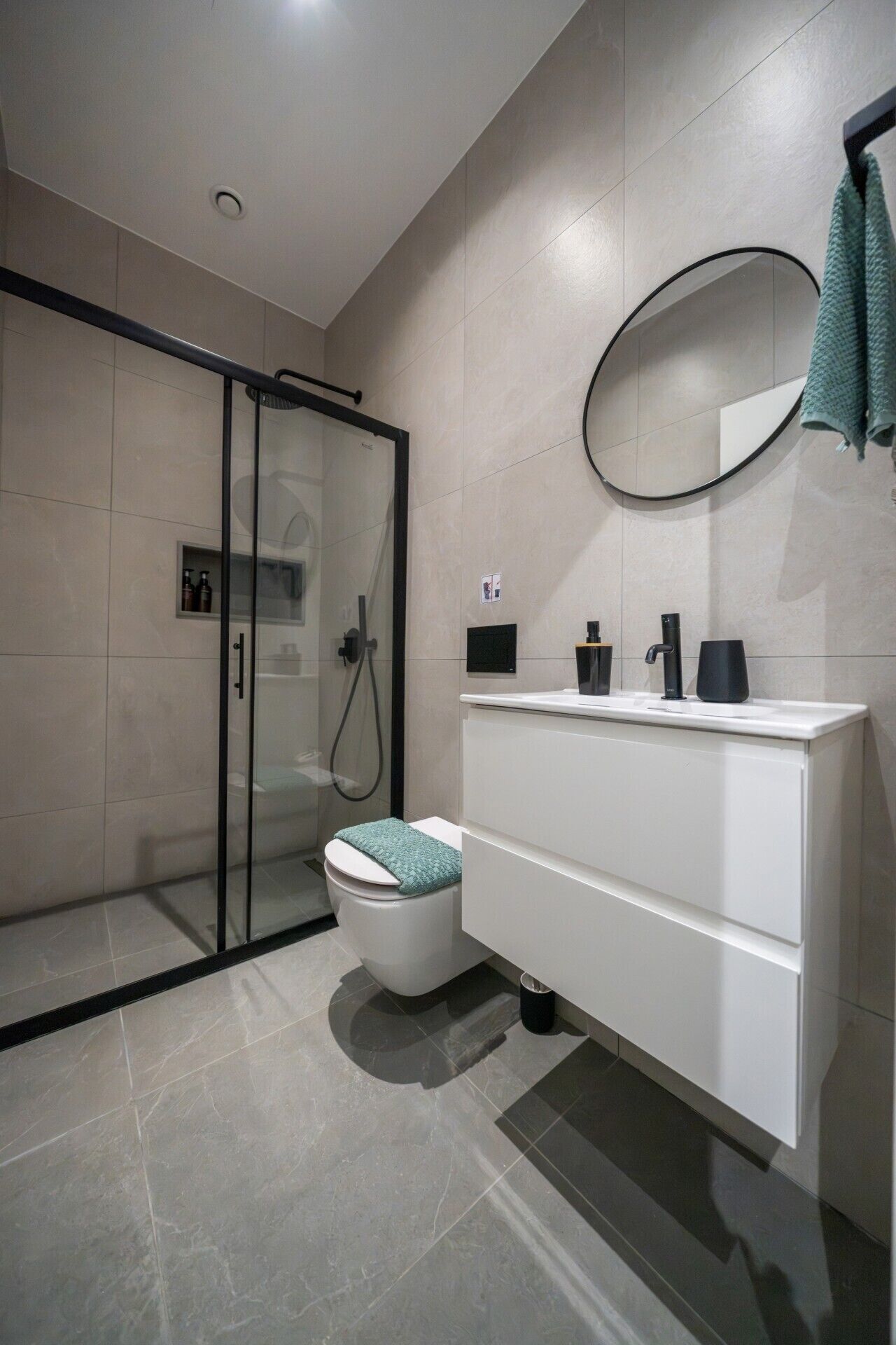 A modern bathroom with a glass shower enclosure, a toilet, a vanity with a mirror, and a towel rack.