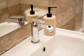 Un baño con grifo cromado, dispensador de jabón color beige y espejo que refleja el lavamanos y la pared.