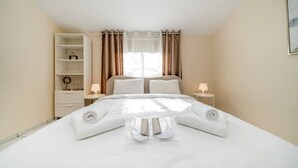 Een hotelkamer met een netjes opgemaakt bed, een nachtkastje met een lamp, een kledingkast en een raam met gordijnen.