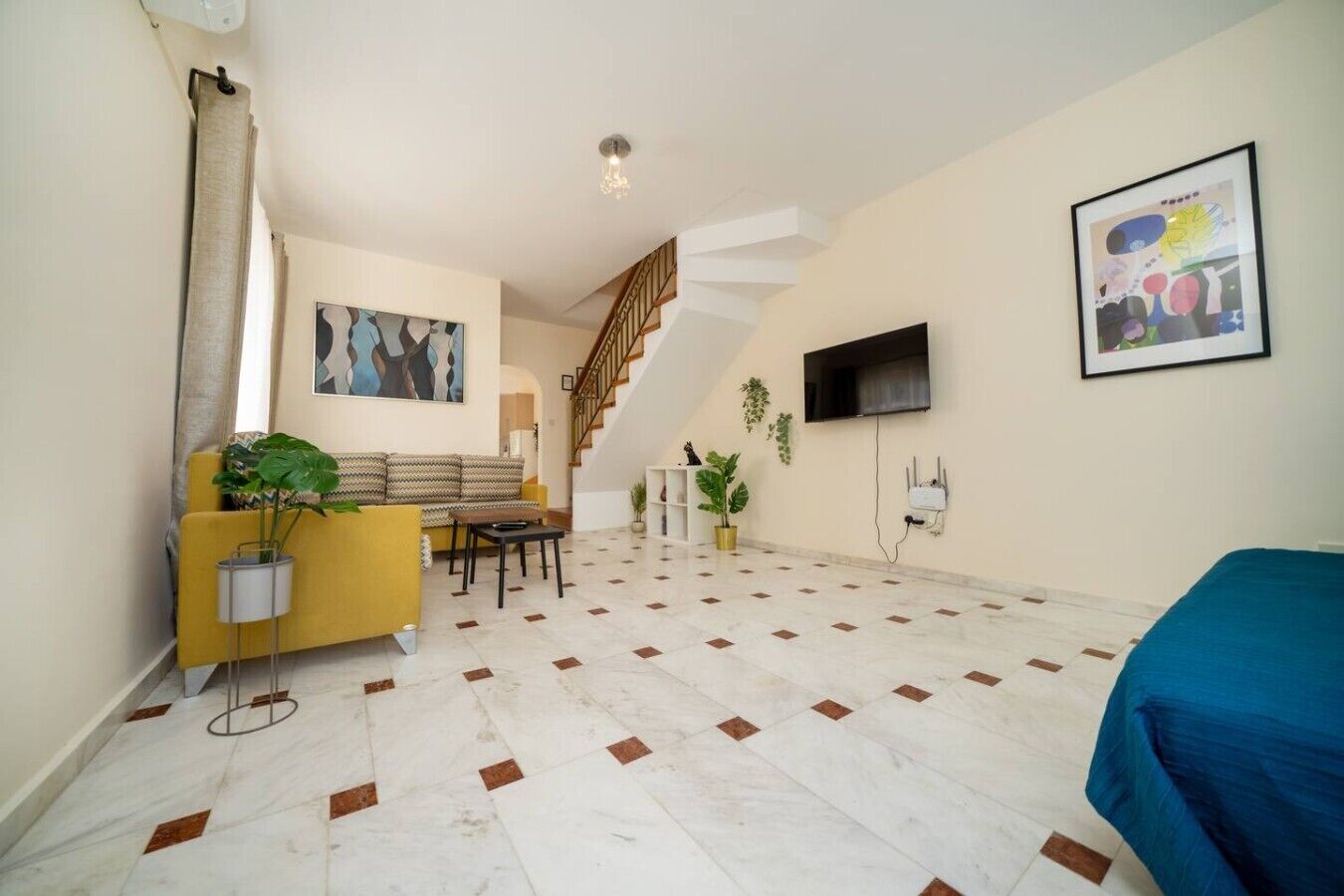 A spacious living area with a sofa, a coffee table, a TV mounted on the wall, and a staircase leading to another level.