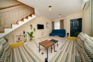 Ein Wohnzimmer mit Treppe, einer Couch, einem Couchtisch und einem Fernseher.
