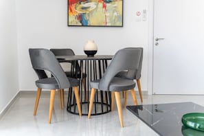 Un coin repas avec une table ronde, quatre chaises grises, un vase et un tableau abstrait aux couleurs vives accroché au mur.