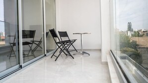 Een balkon met twee stoelen, een kleine tafel, grote glazen deuren en uitzicht over de stad.