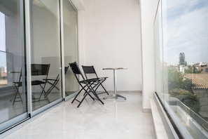Un balcon avec deux chaises et une petite table, de grandes portes vitrées et une vue sur la ville.