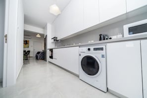 Une cuisine moderne dotée d’un lave-linge et d’un sèche-linge intégrés, de meubles blancs et d’un coin repas à l’arrière-plan.