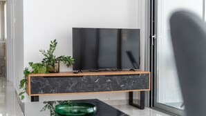 Een moderne woonkamer met een flatscreen televisie op een console van hout en marmer, een groene glazen schaal en een potplant.