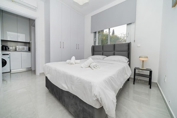 Une chambre à coucher moderne avec un grand lit, une table de chevet, une lampe et une vue sur l’extérieur.