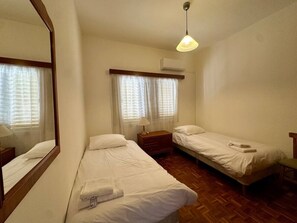 A room with two single beds, a wooden nightstand, a mirror, and a hanging light fixture. - 2 bedroom flat by the sea (Larnaca)