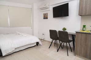 Habitación de hotel con cama, escritorio con dos sillas, televisor de pantalla plana y una planta pequeña.