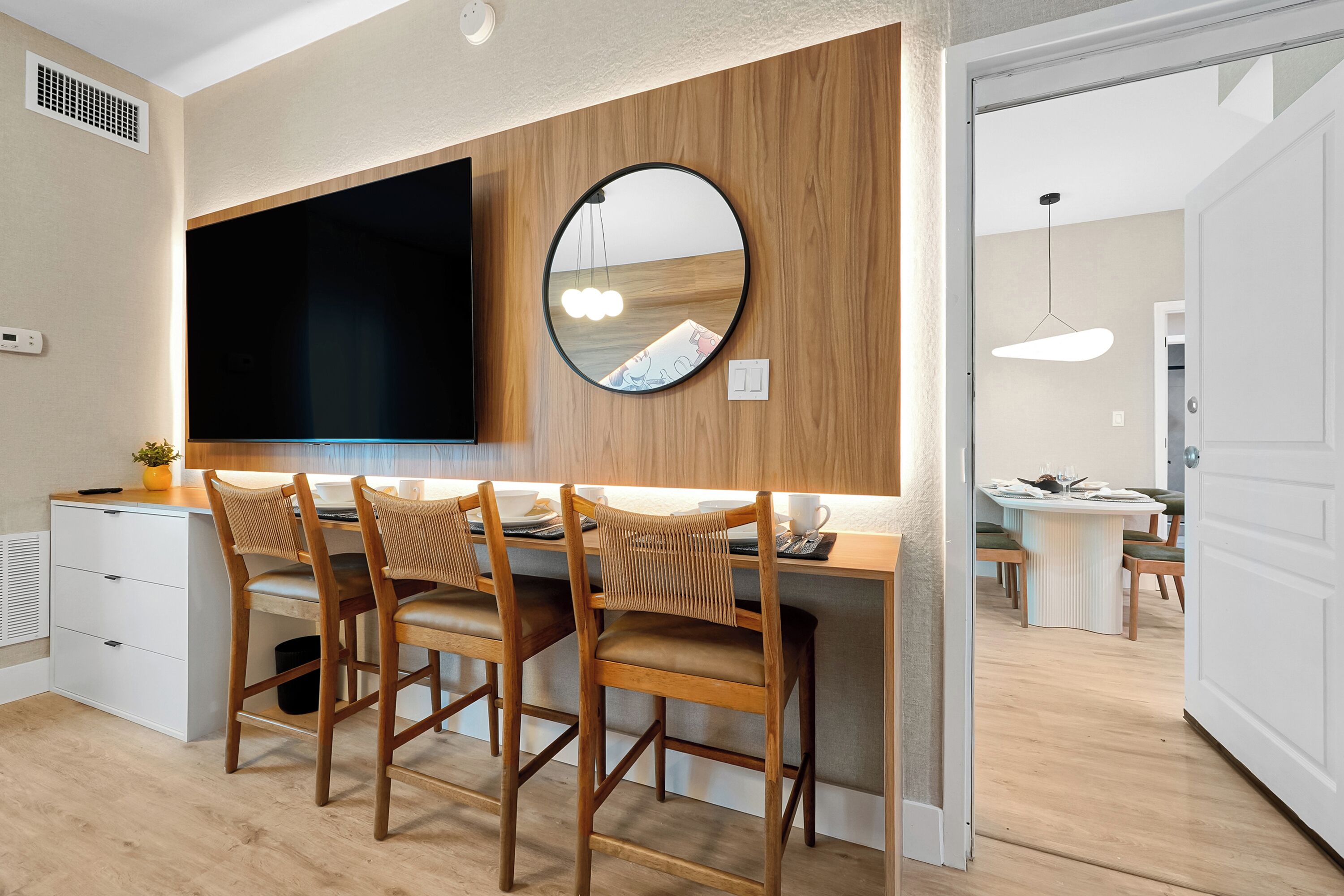A modern kitchen with a wooden island, bar stools, a round mirror, and a dining area with a table and chairs.