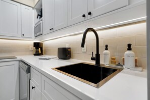 A modern kitchen with a black sink, white cabinets, and a coffee machine. - Apartment and Studio near to Vineland and Disney (Orlando)