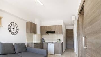 A modern living room with a grey sectional sofa, a kitchen with wooden cabinets, and a wall clock.