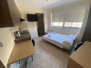 Una habitación pequeña con cama, escritorio, silla, televisión y ventana.