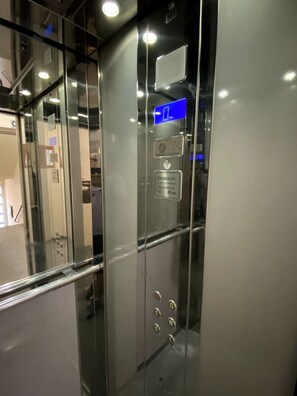 Un ascensor moderno con puertas de vidrio, una pantalla digital y el logotipo de una empresa.