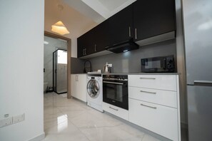A modern kitchen with a washing machine, oven, microwave, and stainless steel refrigerator.