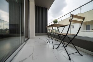 A balcony with a modern design, featuring a glass door, a potted plant, and a wooden table with metal legs.