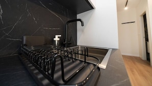 A modern kitchen with a black marble backsplash, a stainless steel sink, and a black towel rack. - New deluxe studio in the heart of Limassol (Limassol)