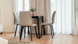 A dining area with a table and four chairs, a vase with flowers, and sheer curtains. - New deluxe studio in the heart of Limassol (Limassol)