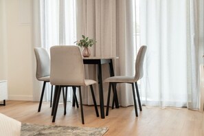 Un comedor con una mesa y cuatro sillas, un florero con flores y cortinas ligeras.