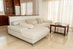 A modern living room with a sectional sofa, a glass coffee table, and a wooden cabinet. - 3 bedroom flat central, beach, walking streets (Limassol)