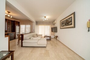 Ein modernes Wohnzimmer mit einer Couch, einem Essbereich, einer Küche und einem an der Wand montierten Fernseher.