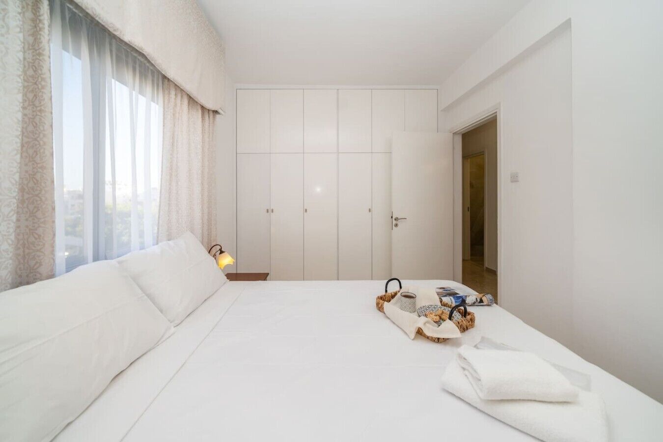 A hotel room with a bed, a bedside table, a lamp, a wardrobe, and a window with curtains.
