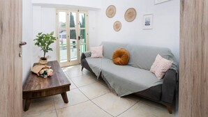 Una sala de estar con un sofá gris, una mesa de centro de madera, una planta en maceta y una puerta que da a un área exterior.