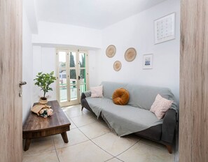 A living room with a grey sofa, a wooden coffee table, a potted plant, and a door leading to an outdoor area. - Private room in shared flat (Nicosia)