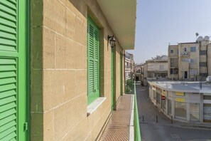 Eine schmale Straße mit Häusern, einem Balkon mit grünen Fensterläden und einem Schild mit der Aufschrift 'ACCESSORIES'.
