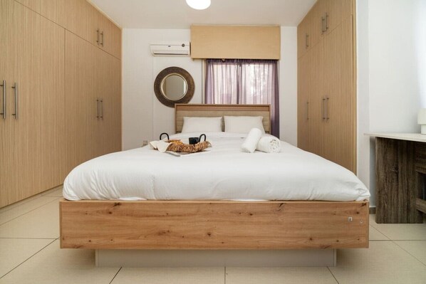 A bedroom with a wooden bed frame, a round mirror, a bedside table, and a window with curtains.