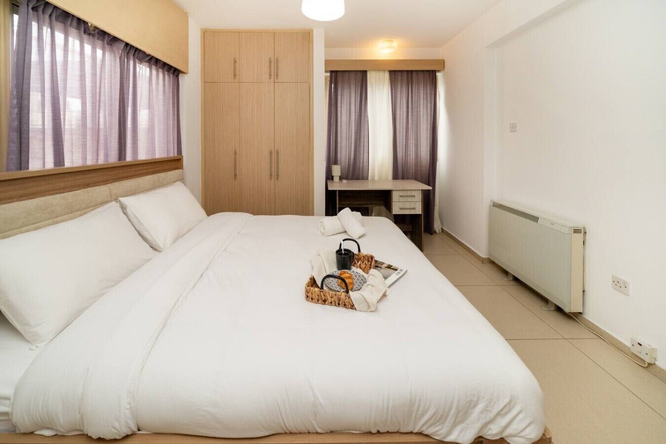 A hotel room with a large bed, a desk, a wardrobe, and a radiator.