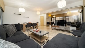 A modern living room with a sofa, coffee table, TV, and dining area. - 3 bedroom flat near center (Nicosia)