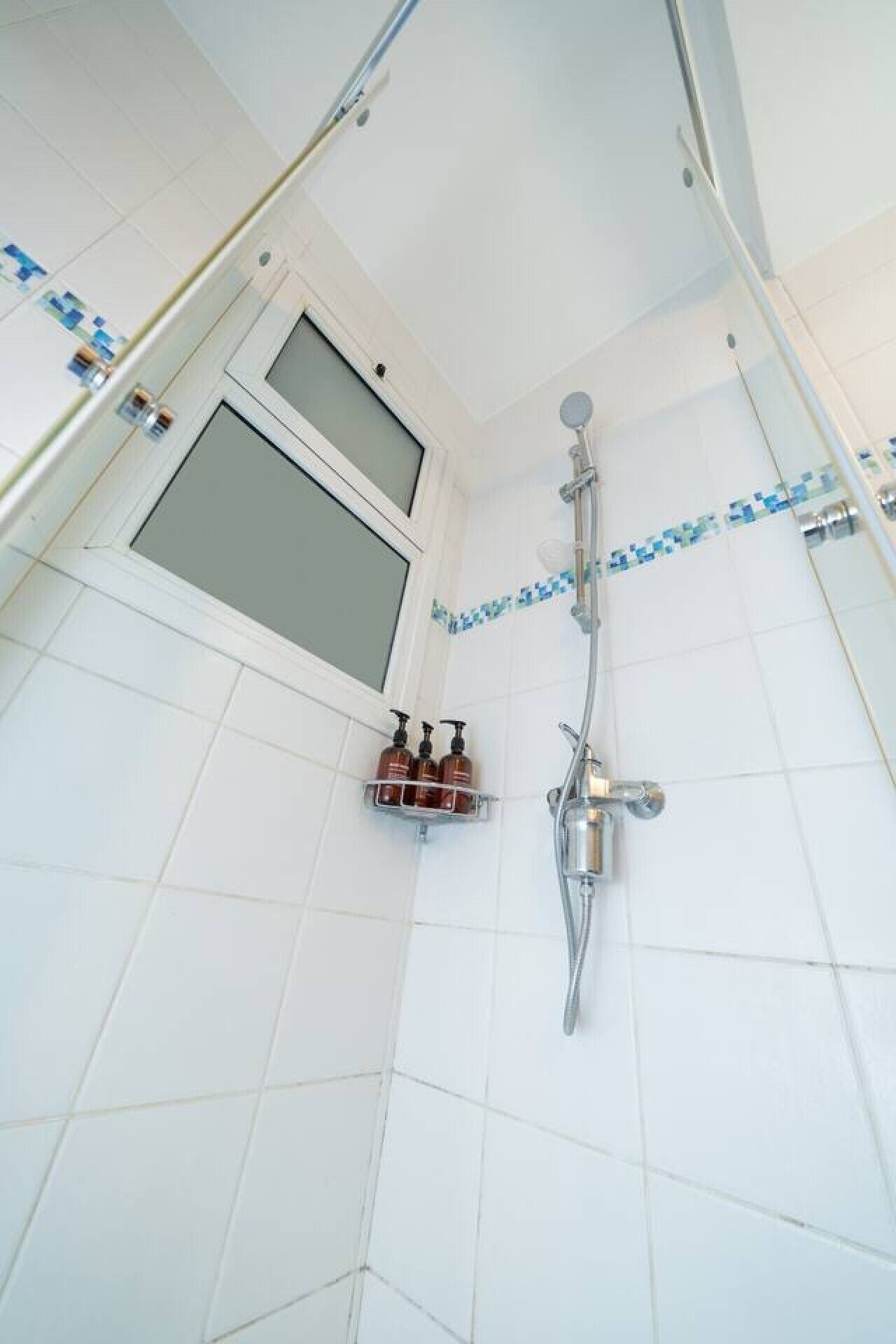 Une douche avec une porte en verre, un pommeau de douche à main et un robinet fixé au mur.