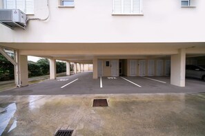 Un parking souterrain avec des places de stationnement numérotées, une grille d’évacuation et un bâtiment doté de fenêtres et d’un appareil de climatisation.