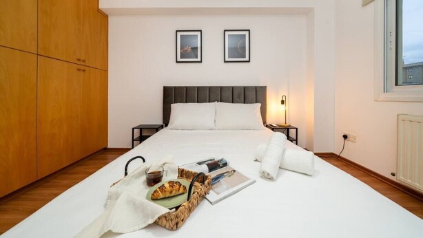 Cama bem arrumada com uma bandeja de itens de café da manhã, mesa de cabeceira com abajur e um guarda-roupa grande.