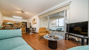 Uma sala de estar moderna com sofá, mesa de centro, televisão e uma área de jantar com cadeiras e mesa.