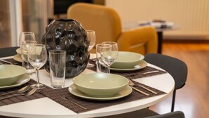 Uma mesa de jantar posta com pratos, copos e talheres, rodeada por cadeiras.