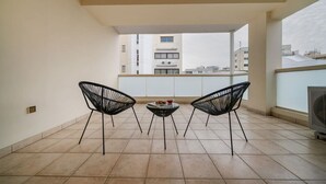 Uma varanda com duas cadeiras pretas, uma mesinha e uma televisão.