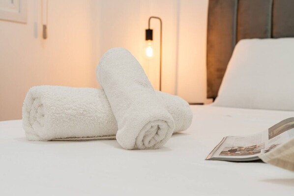 A neatly made bed with two rolled white towels and a magazine on it.