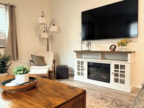 Ein Wohnzimmer mit Flachbildfernseher, weißem Unterhaltungsschrank, Holztisch und weißem Sessel.