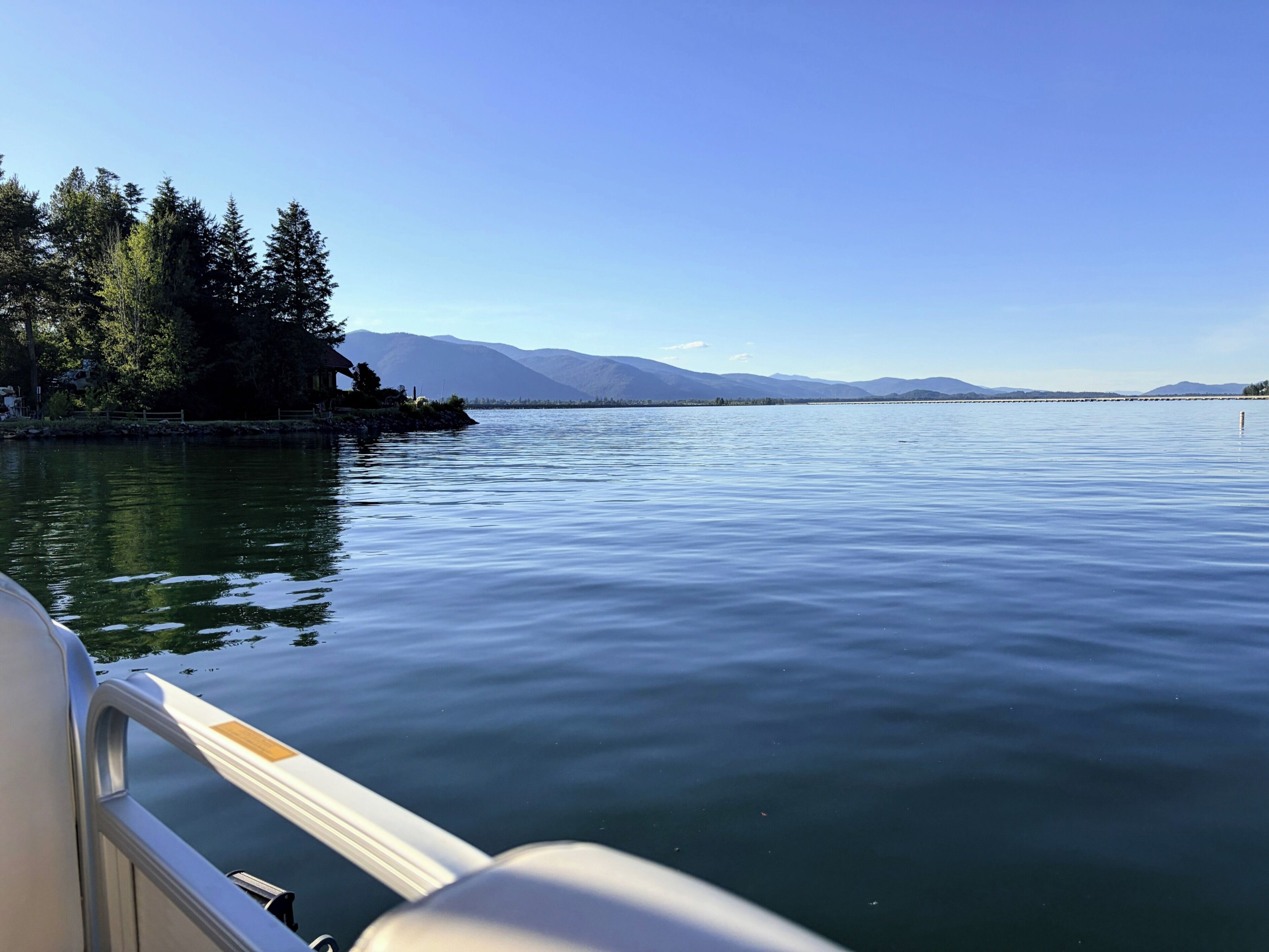 Un lac paisible, avec un bateau au premier plan, entouré d’arbres et de montagnes à l’horizon.