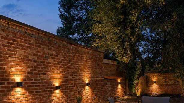 Un patio al aire libre con paredes de ladrillo, mobiliario exterior e iluminación instalada en las paredes.