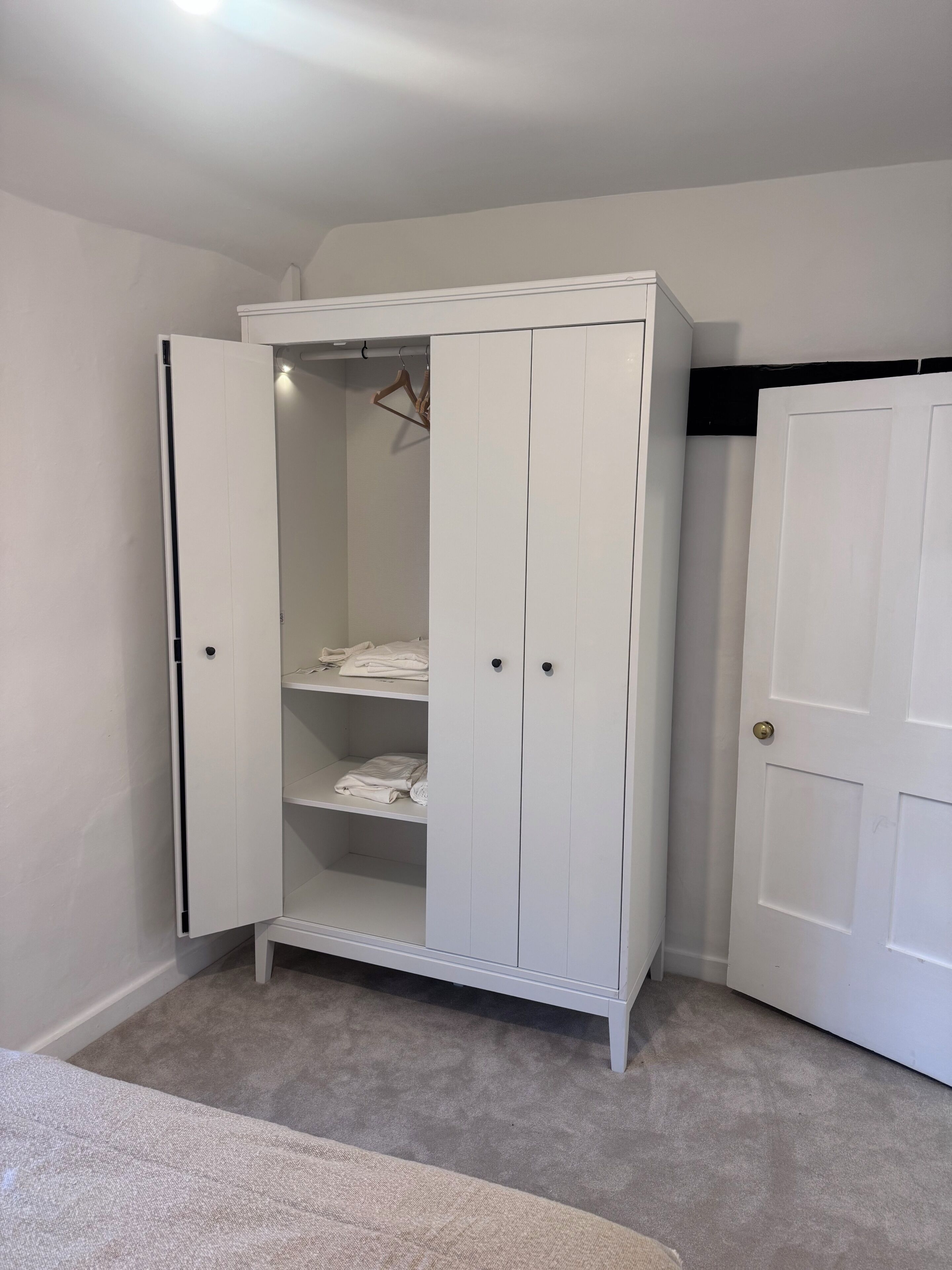 Ein weißer Kleiderschrank mit zwei Türen, einer Kleiderstange und einem Einlegeboden.