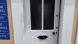 Una puerta blanca con pomo negro, una ventana con vidrio esmerilado y un letrero azul en la pared.