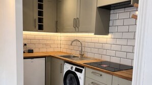 Cocina compacta con armarios grises, lavadora y encimera de madera.