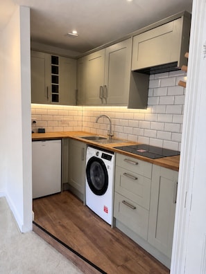 Une cuisine de taille réduite avec des meubles gris, un lave-linge et un plan de travail en bois.