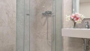 A bathroom with a glass-enclosed shower, a white sink, and a mirror.