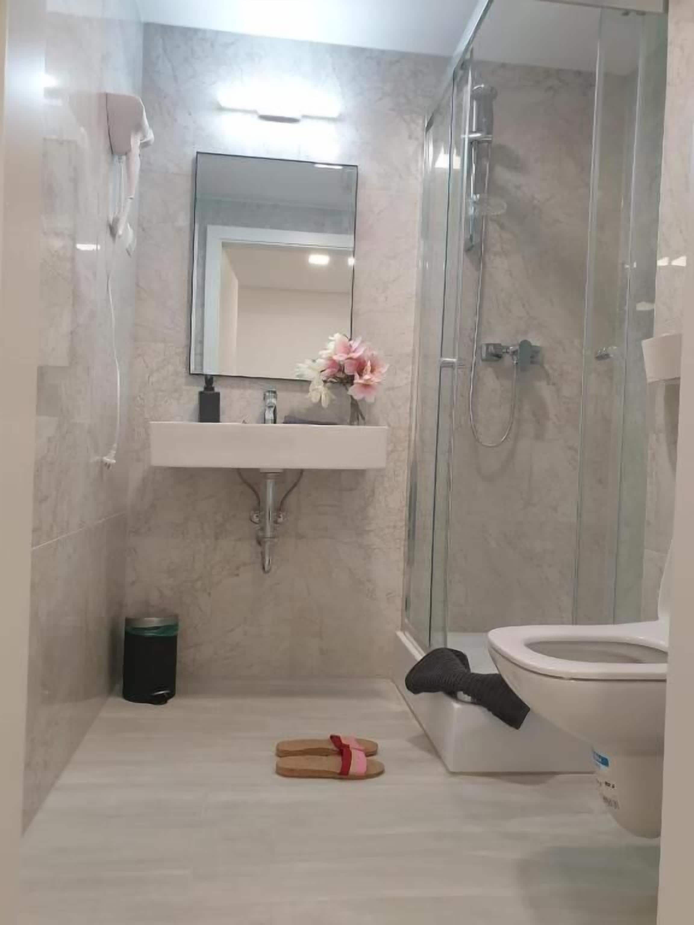 A bathroom with a glass shower enclosure, a white sink with a mirror, and a toilet.