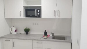 A modern kitchen with white cabinets, a microwave, a kettle, and a sink.