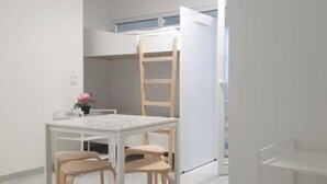 A modern, minimalistic room with a white table, chairs, a ladder, and a white shelving unit.